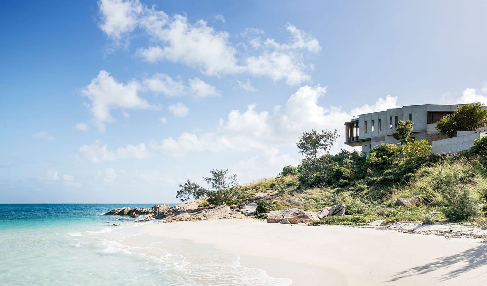 A modern house above a white sand beach and turquoise water