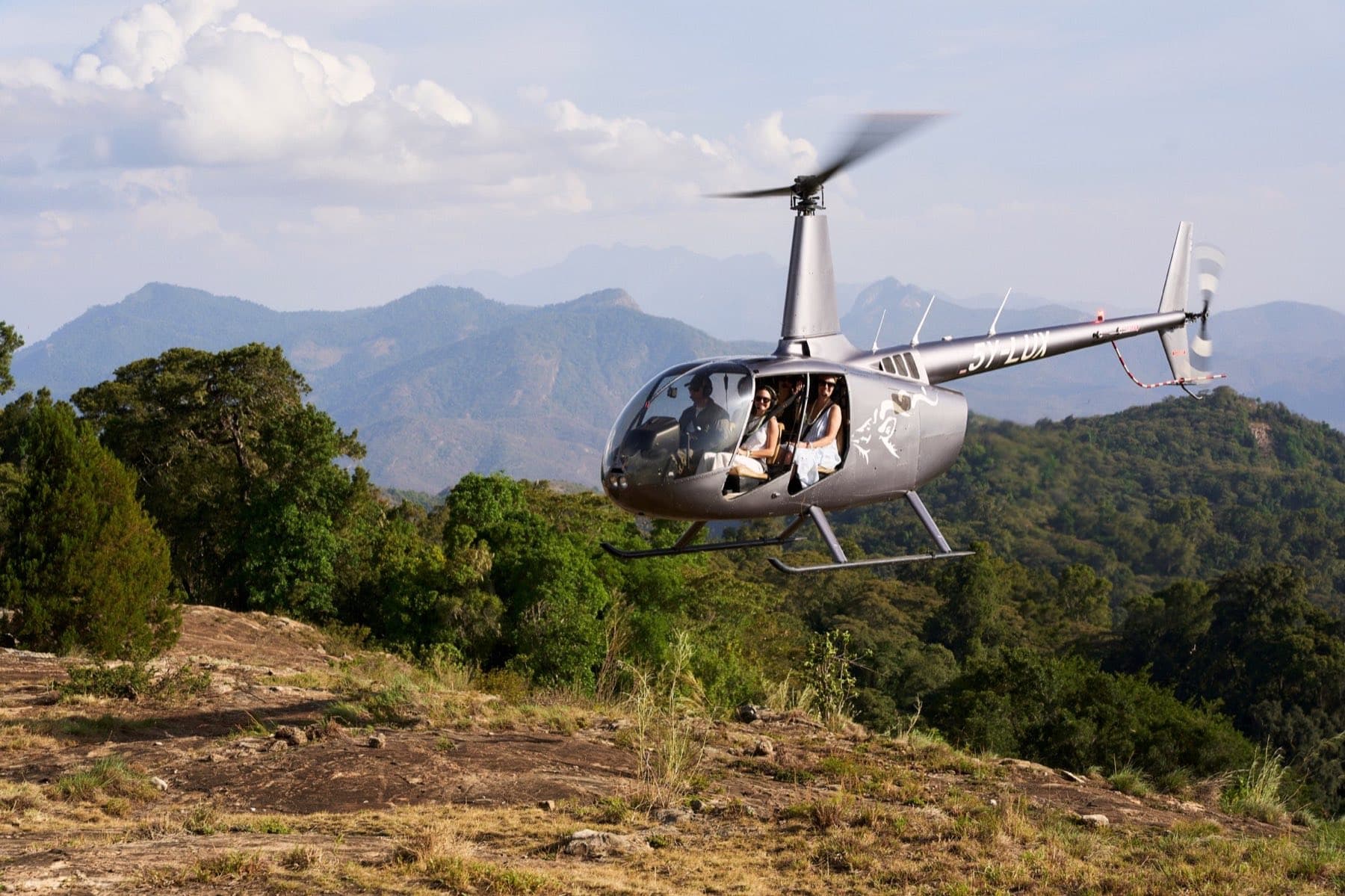 A helicopter with passengers lifting off a forested mountainside