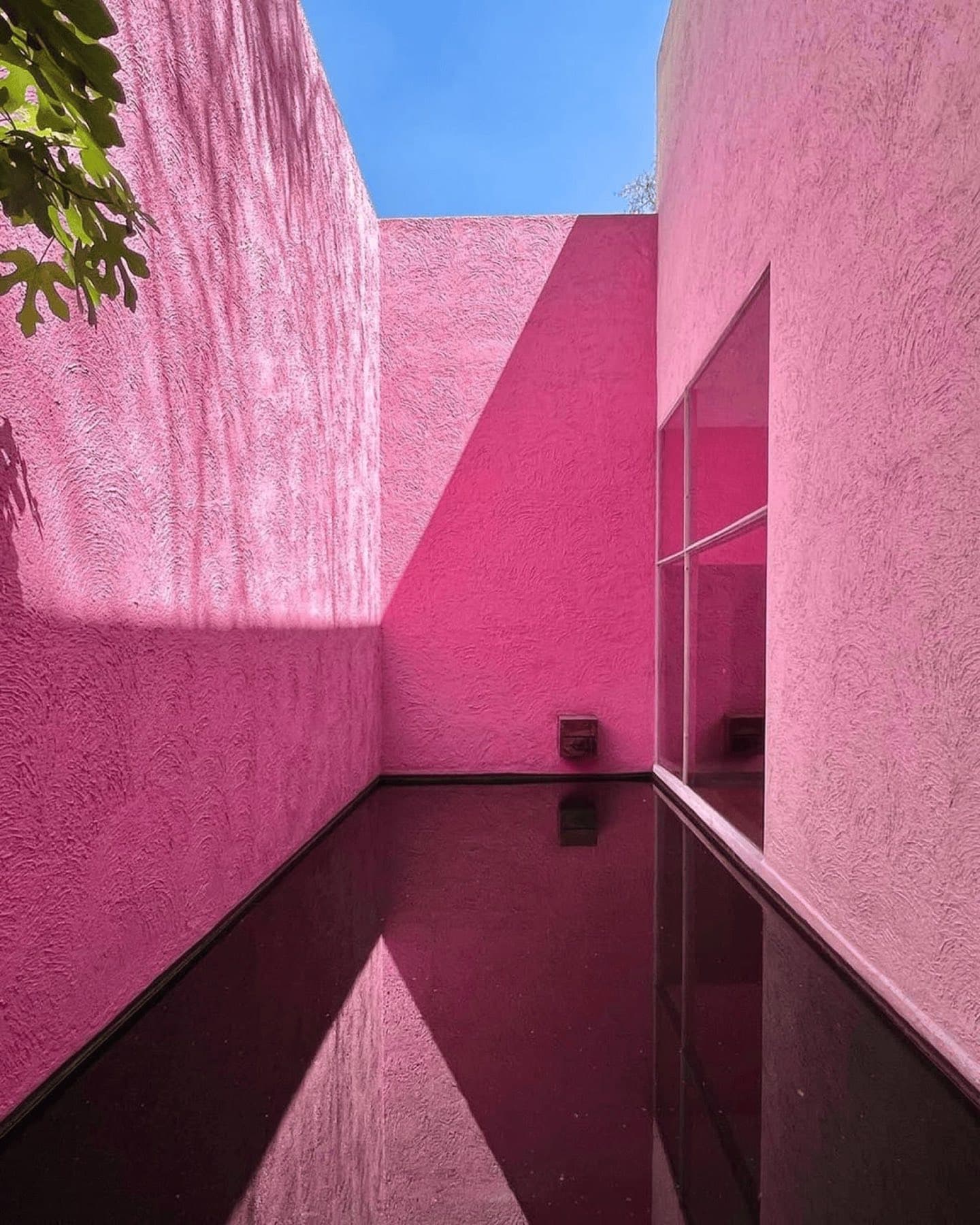 A pink courtyard with a still pool reflecting the walls