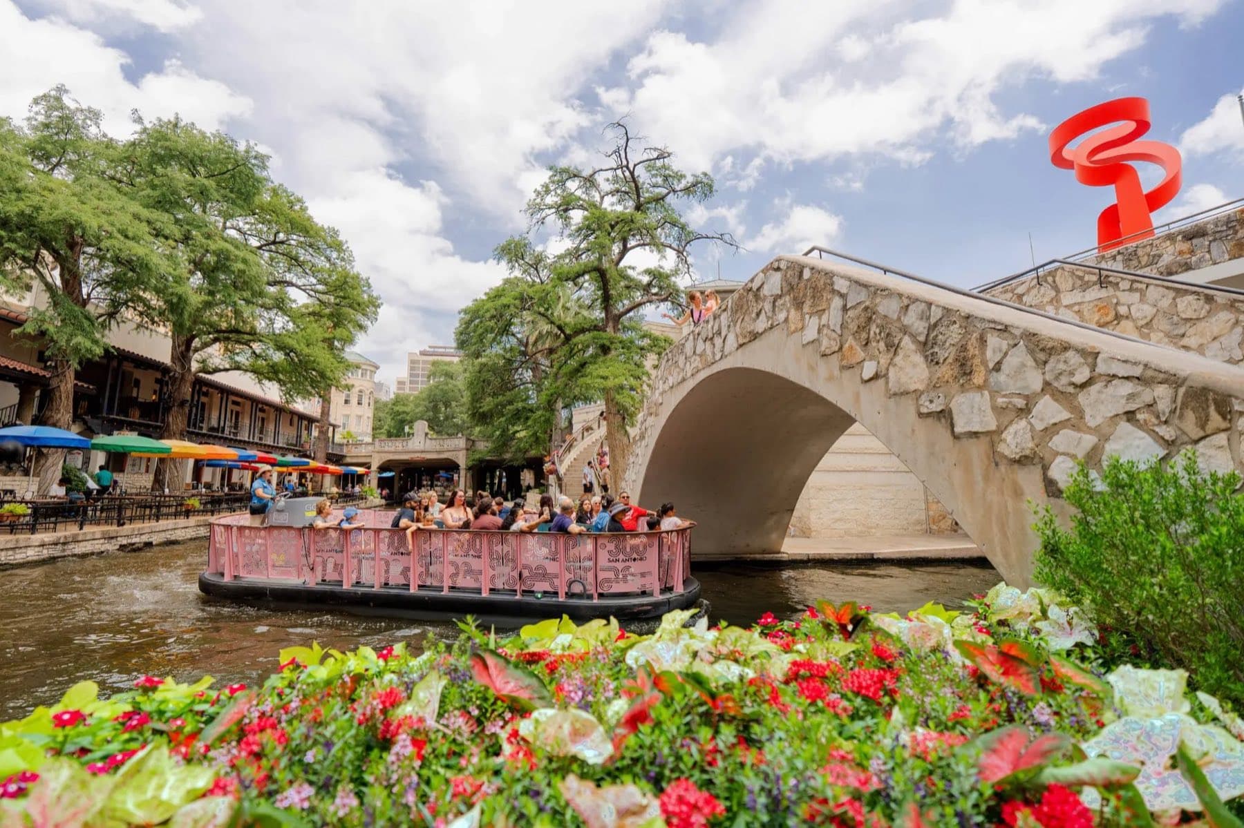 A riverside walk with flowers and a stone bridge