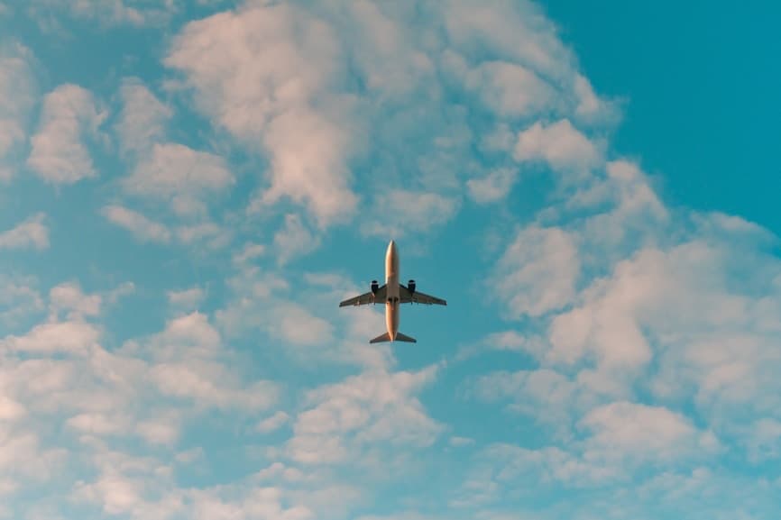 An airliner seen from below against a blue sky with soft clouds