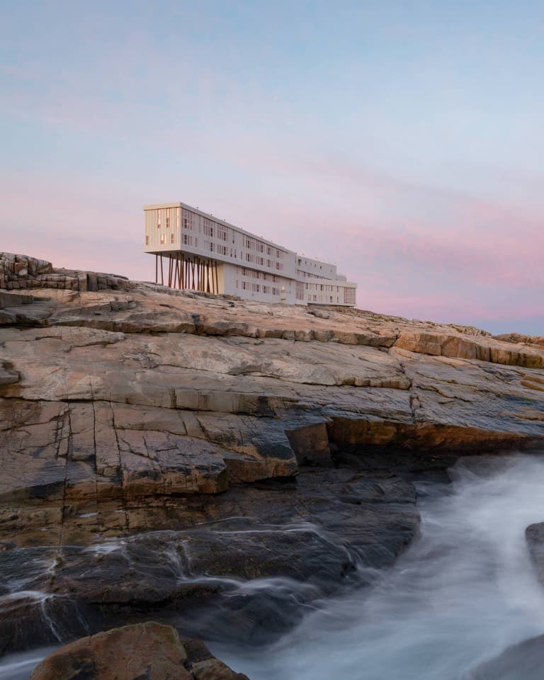 A long white inn on stilts over rocks at dusk